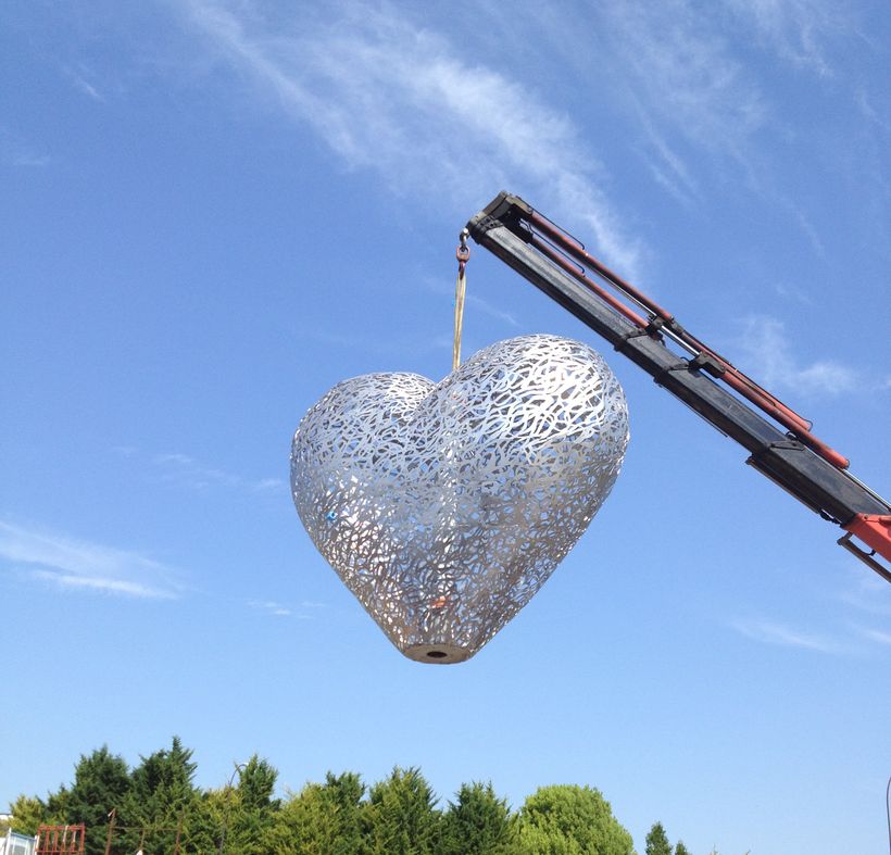 Le cœur d'inox ajouré suspendu à la grue, seul dans le ciel bleu
