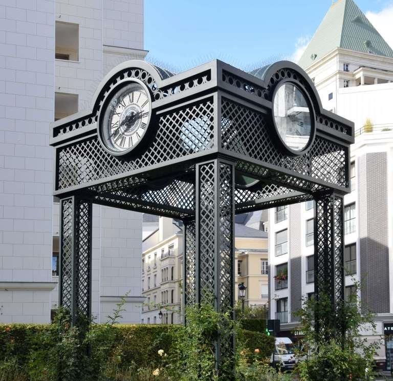 Kiosque-horloge en treillis d'acier vert au milieu d'une roseraie